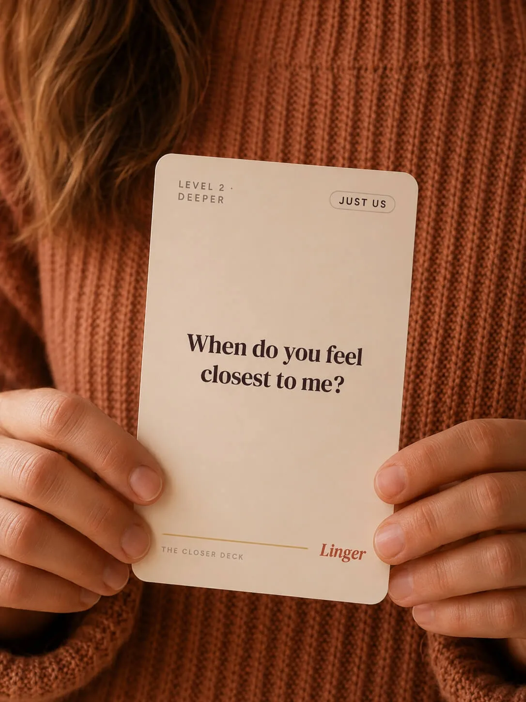 A woman holding a Linger Closer Deck card that reads 'When do you feel closest to me?'